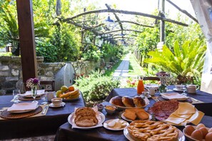An outdoor dining area with a variety of food items, including bread, pastries, and eggs, set against a backdrop of greenery and a stone wall. - Agriturismo Il Convento (Massa Lubrense)