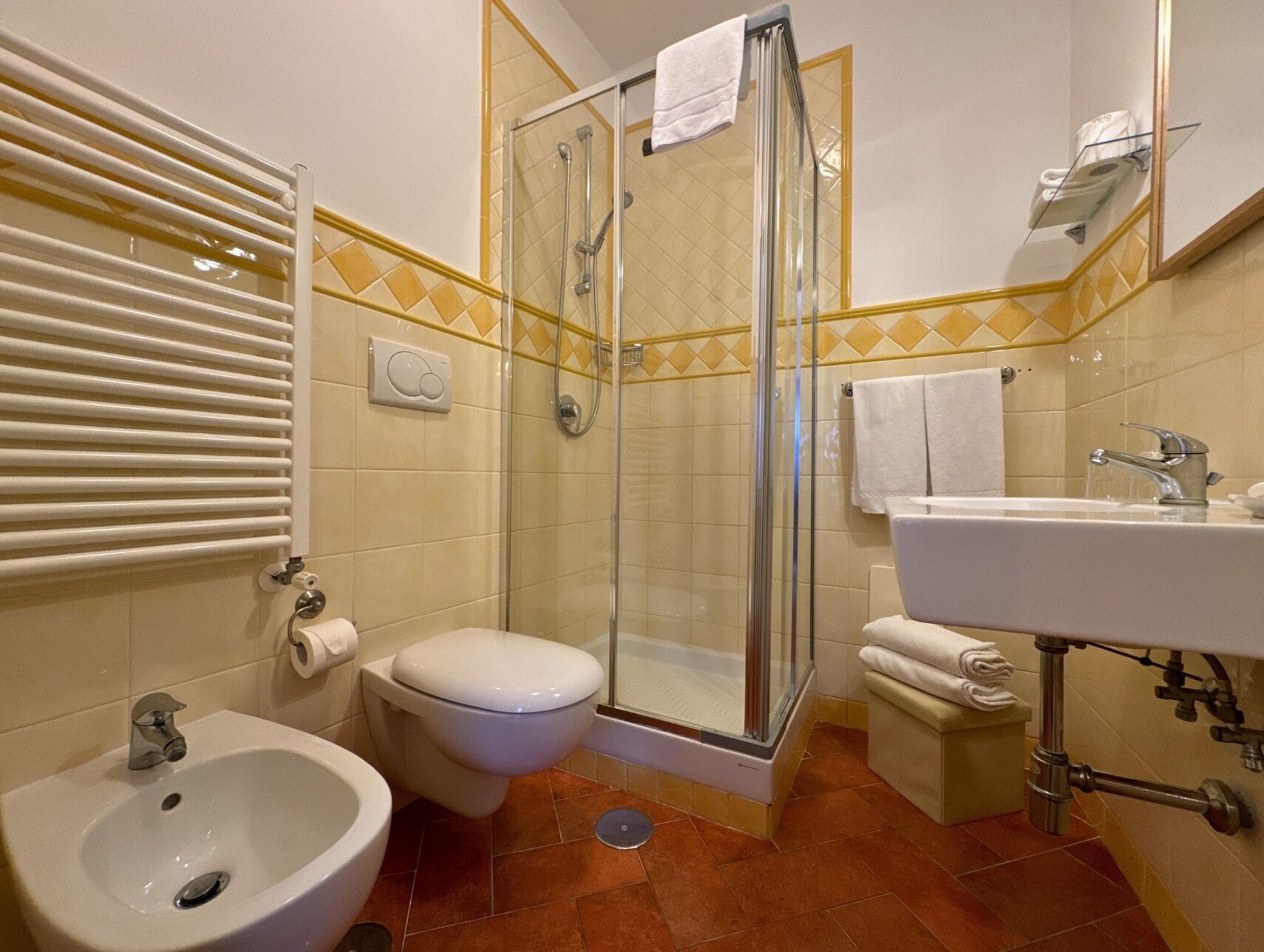 Casa de banho com chuveiro, sanita, bidé, lavatório e porta-toalhas.