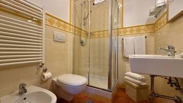 Casa de banho com chuveiro, sanita, bidé, lavatório e porta-toalhas.