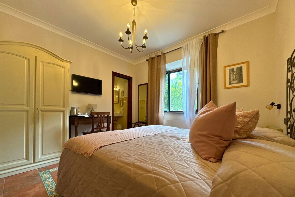Ein Schlafzimmer mit einem großen Bett, einem Schreibtisch mit Stuhl, einem Fernseher und einem Fenster mit Vorhängen.