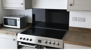 A kitchen with a stainless steel stove, a microwave, and white cabinets. - Iffley Town House (Oxford)