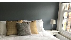 A neatly made bed with white bedding and multiple pillows in a room with a dark wall and a window with blinds. - Iffley Town House (Oxford)