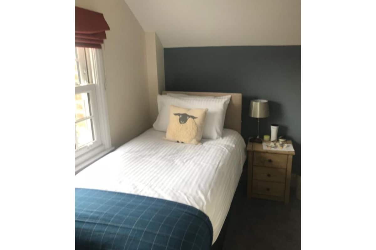 A bedroom with a bed, a nightstand, a lamp, and a window with curtains.