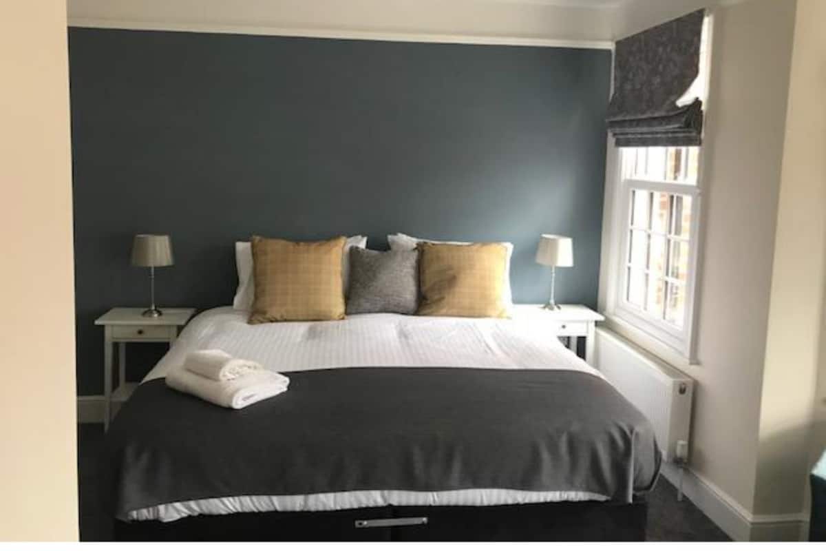 A neatly made bed with a dark headboard, two bedside tables with lamps, and a window with a view.