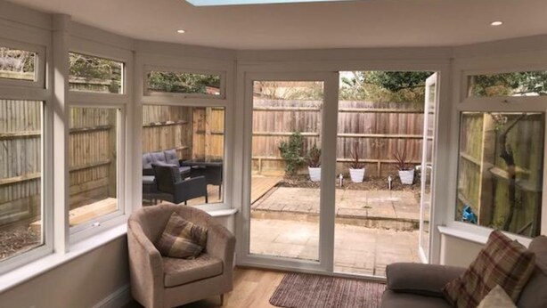 A sunlit room with a large sliding glass door leading to a backyard. Inside, there is a beige sofa and a chair. - Iffley Town House (Oxford)