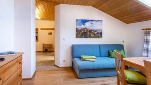 Una habitación acogedora con techo de madera, un sofá azul, una mesa de madera y un cuadro de un paisaje montañoso.