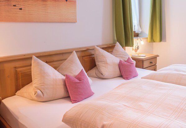 Una habitación de hotel con cabecera de madera, dos camas con almohadas a juego, una mesita de noche con lámpara y cortinas verdes.