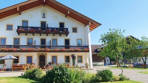 Ein mehrstöckiges Gebäude mit einem mit Blumen geschmückten Balkon, einer überdachten Außenbereich-Sitzgelegenheit und einem Vorgarten.