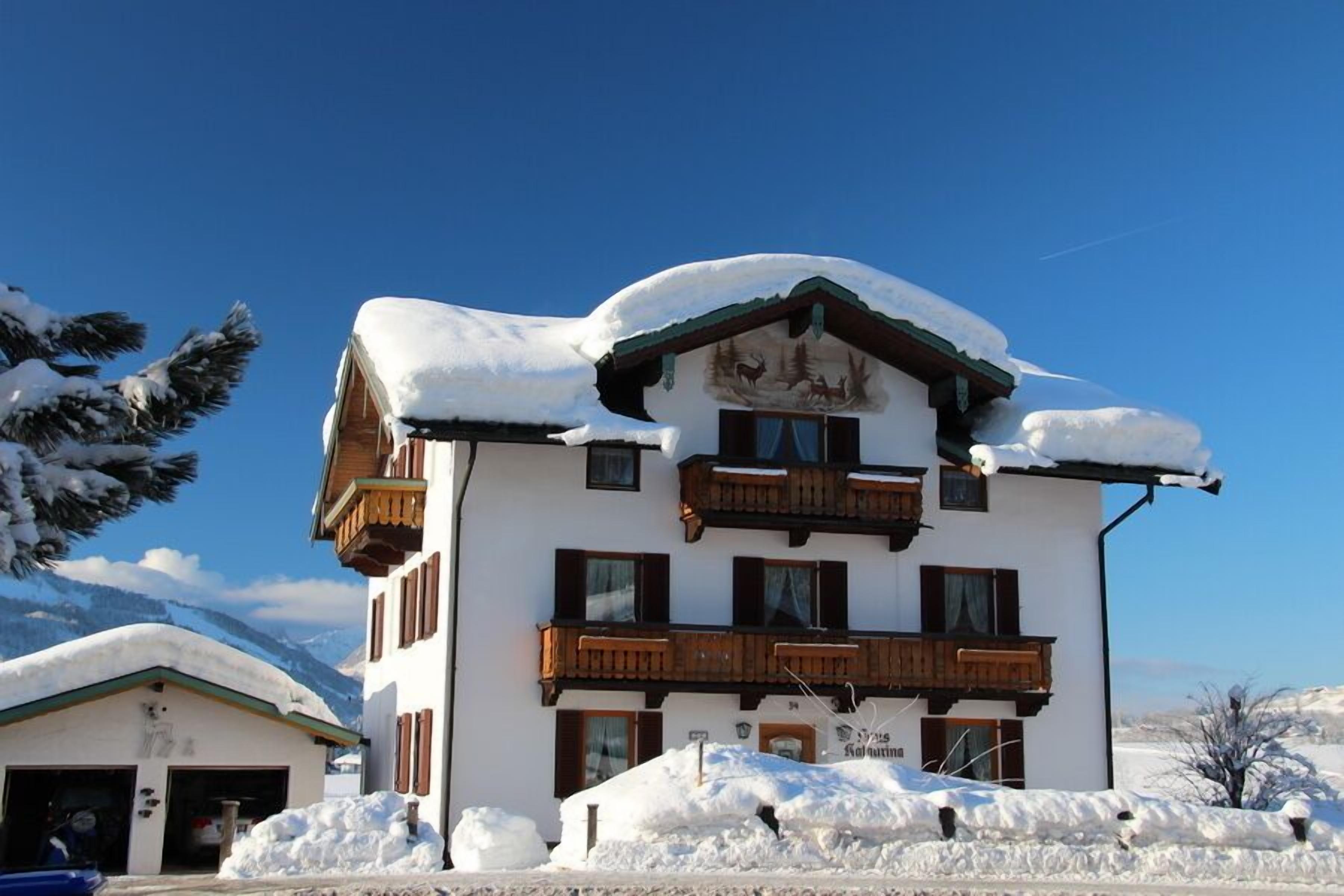 A multi-story building with a snow-covered roof and balconies, surrounded by snow.