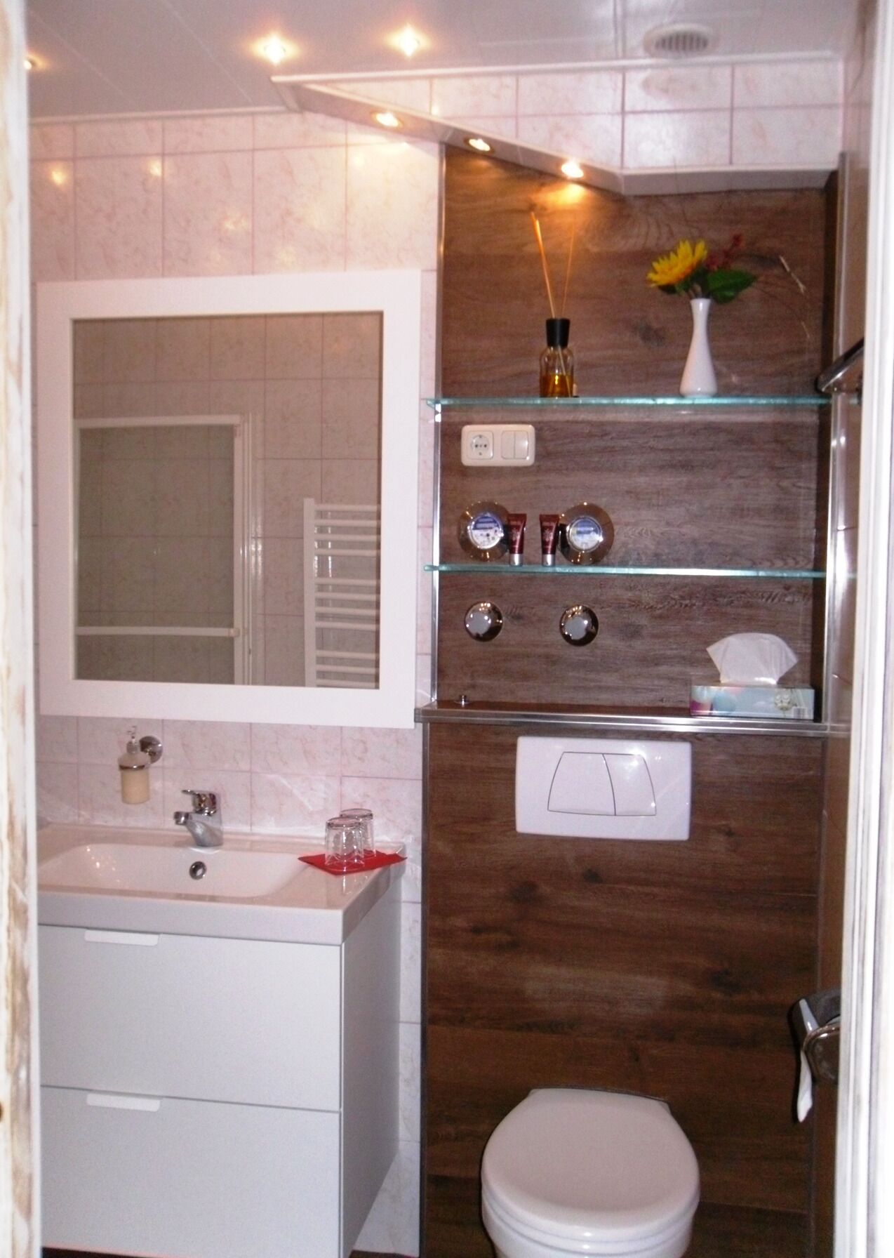 A modern bathroom with a marble vanity, a glass shelf with toiletries, a wooden accent wall, and a white toilet.