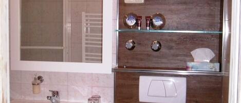 A modern bathroom with a marble vanity, a glass shelf with toiletries, a wooden accent wall, and a white toilet.