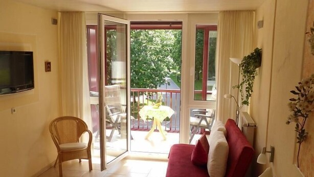 A hotel room with a bed, a chair, a red sofa, and a balcony with a table and chairs. - sonnige, ruhige, zentrale Ferienwohnung mit Bergblick am Rupertuspark (Bad Reichenhall)