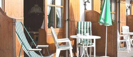 An outdoor seating area with a table and chairs, a green umbrella, and wooden shutters.