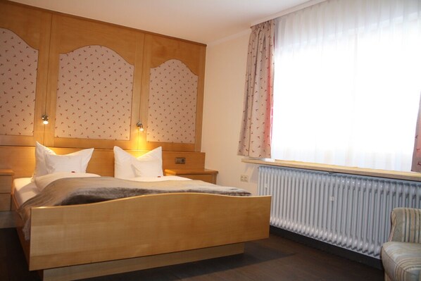 A hotel room with a wooden bed, a nightstand, a dresser, and a radiator.