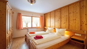 A wooden room with a large bed, a window with curtains, and a wooden wardrobe.