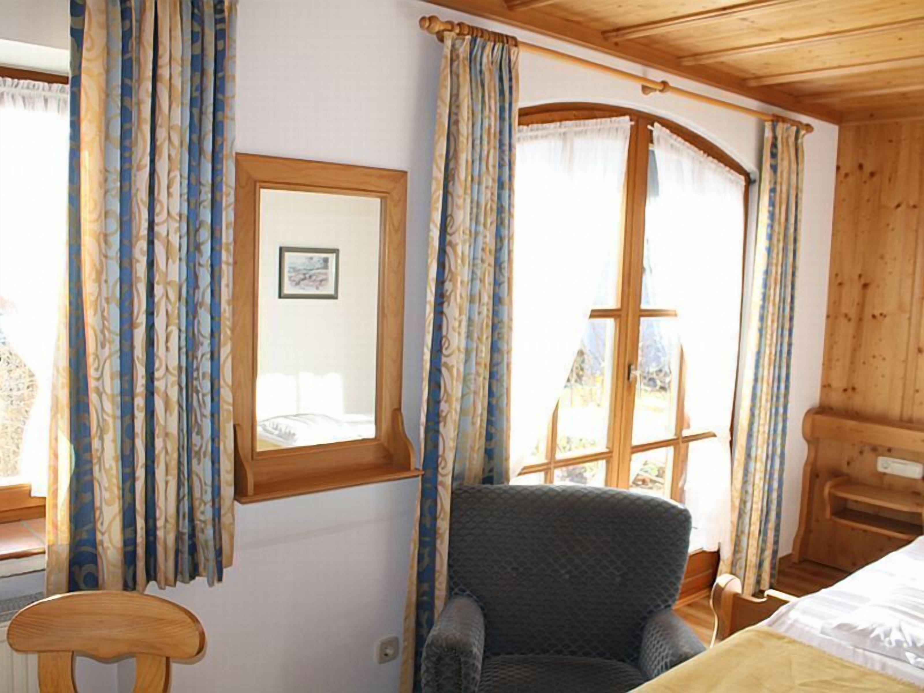 Una habitación con una cama, una silla, un escritorio de madera y una ventana con cortinas.