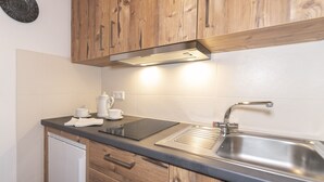 Une cuisine avec des meubles de rangement en bois, un évier en acier inoxydable, une cuisinière encastrée et une bouilloire.
