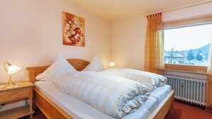 Quarto com cama de madeira, duas luminárias de cabeceira, radiador e janela com cortinas.
