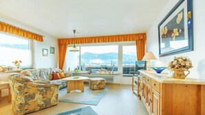 Uma sala de estar aconchegante com sofá, mesa de centro e vista para montanhas por grandes janelas.