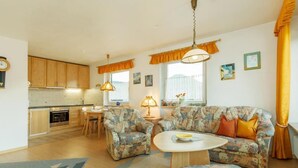 Uma sala de estar acolhedora com sofás de padrão floral e uma mesa de centro, uma cozinha com armários de madeira e uma área de jantar com mesa e cadeiras.