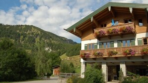Un bâtiment en bois à deux étages, doté de balcons ornés de fleurs, se dressant sur un fond de montagnes.