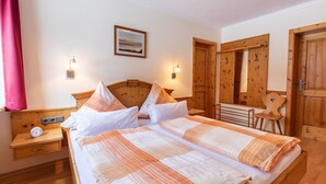 Un lit double avec une couvre-lit à rayures, une table de chevet avec une horloge et une petite table de nuit. Il y a deux lampes fixées au mur et un tableau encadré accroché au mur.