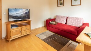Un salon avec un canapé rouge, un meuble de rangement en bois et un téléviseur à écran plat.