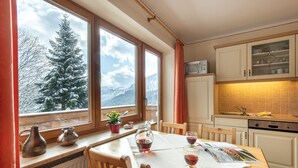 Une cuisine comprenant une table à manger, des chaises, une fenêtre donnant sur des arbres couverts de neige et des placards.