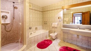 Ein Badezimmer mit Dusche, Badewanne und Waschbecken, mit gefliestem Boden und einem Spiegel über dem Waschbecken.