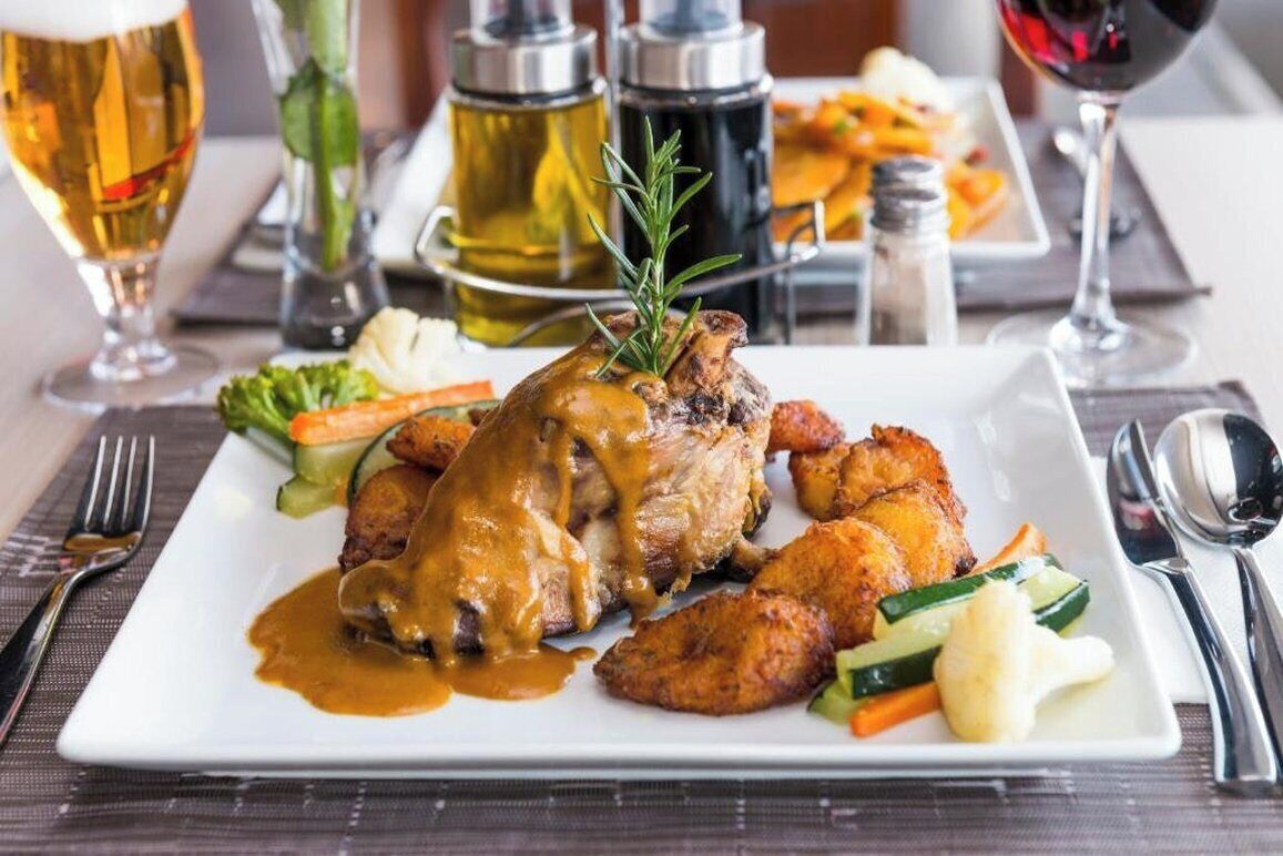 A plated meal with roasted chicken, gravy, and vegetables, accompanied by a glass of beer and a glass of red wine.