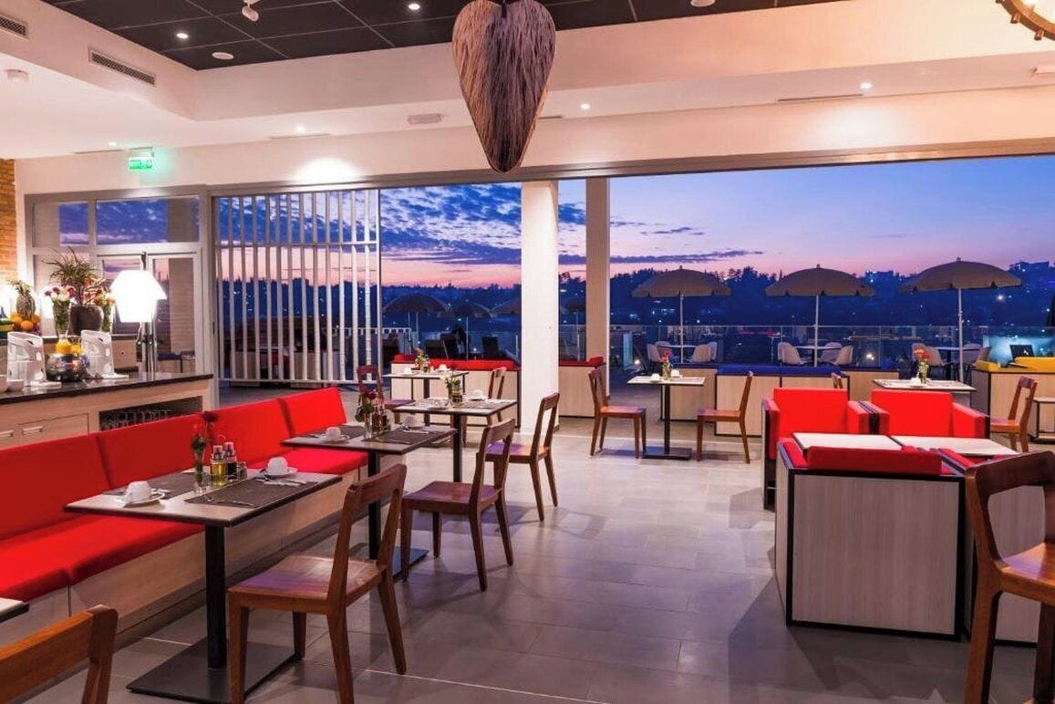 A restaurant with a terrace, red seating, and a view of the city at dusk.
