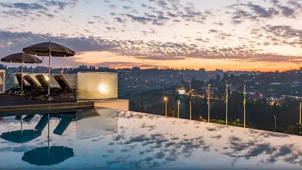 Une piscine à débordement avec des chaises longues et des parasols, offrant une vue sur le paysage urbain au coucher du soleil.