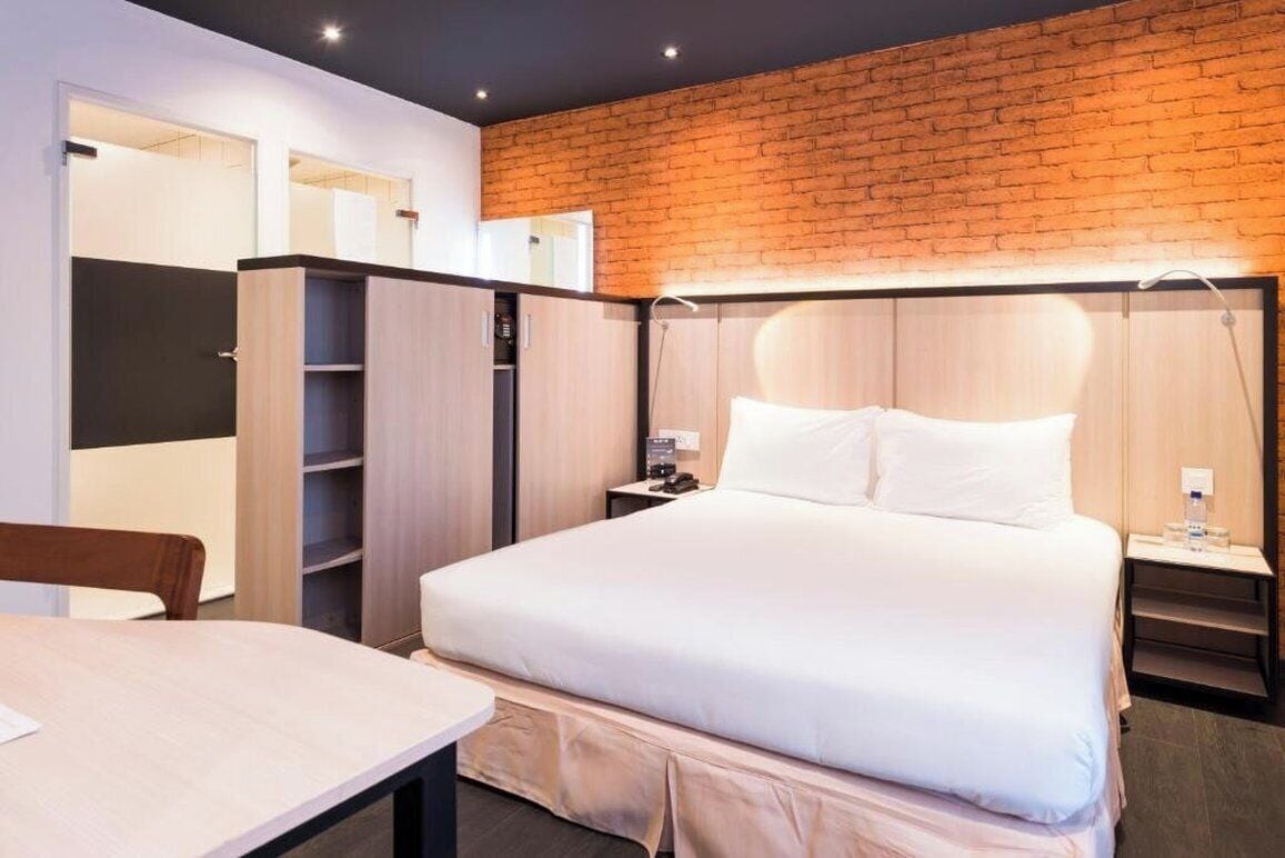Een hotelkamer met een bed, een bureau, een kledingkast en een bakstenen muur.