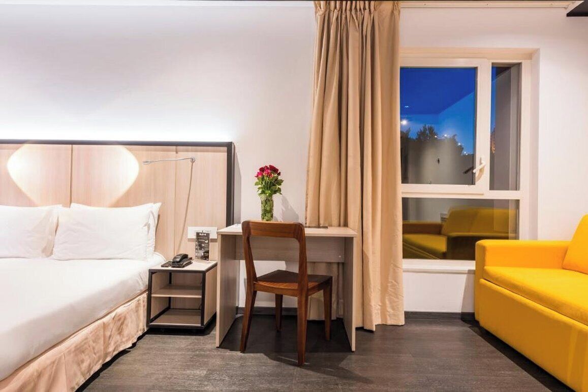 Habitación de hotel con cama, escritorio, silla y ventana con cortinas.