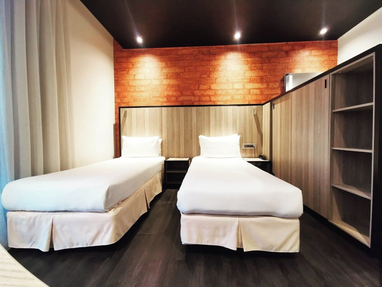 A hotel room with two single beds, a wooden accent wall, and a wardrobe.