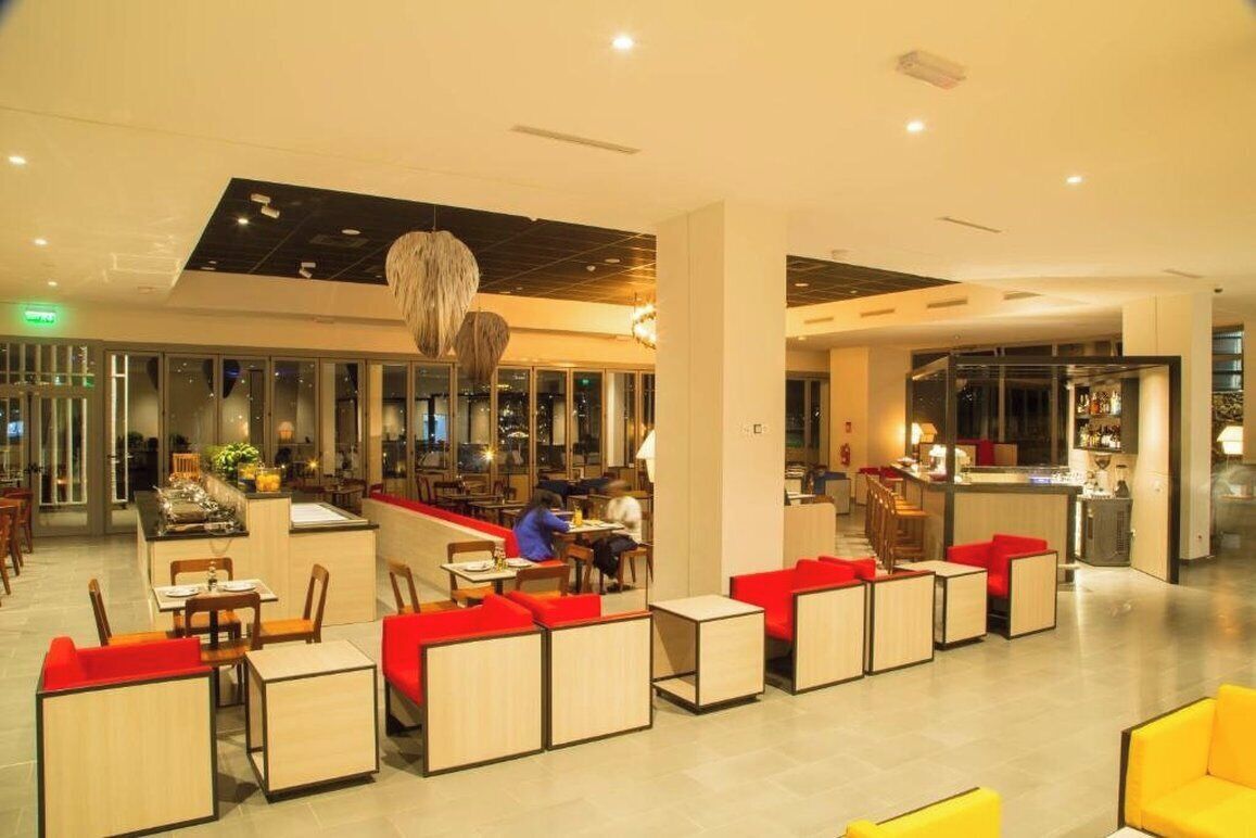 A modern hotel lobby with seating areas, a bar, and a view of the city at night.