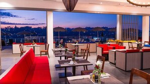 Un restaurant situé sur le toit d’un immeuble, avec une terrasse, de grandes fenêtres et une vue sur la ville au crépuscule.