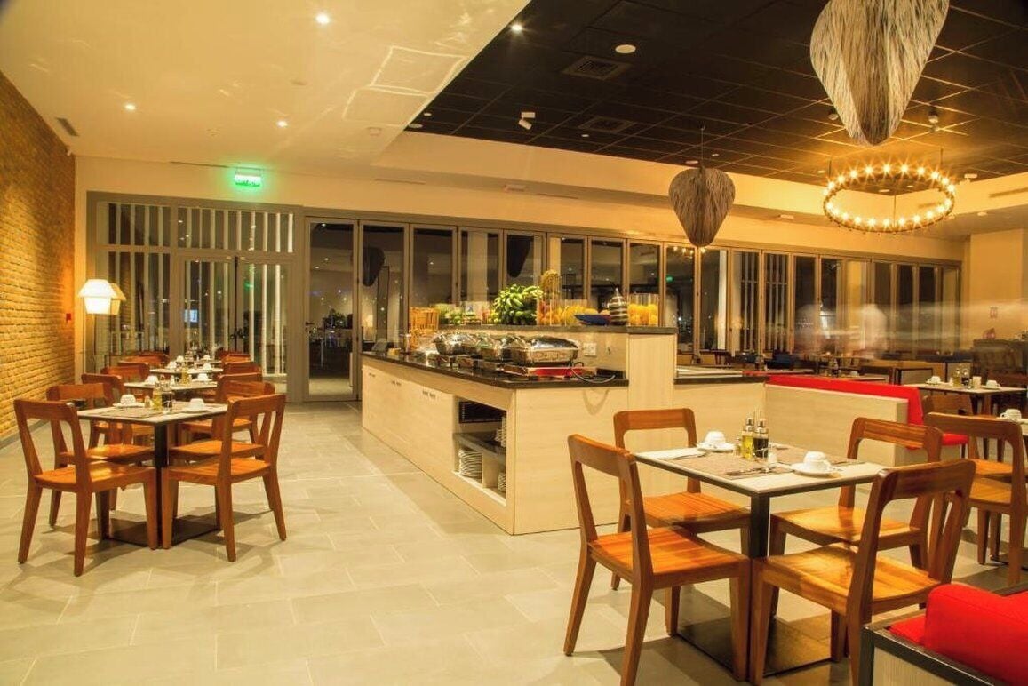 A restaurant with wooden tables and chairs, a central buffet area, and a modern chandelier.