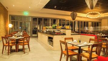 A restaurant with wooden tables and chairs, a central buffet area, and a modern chandelier.