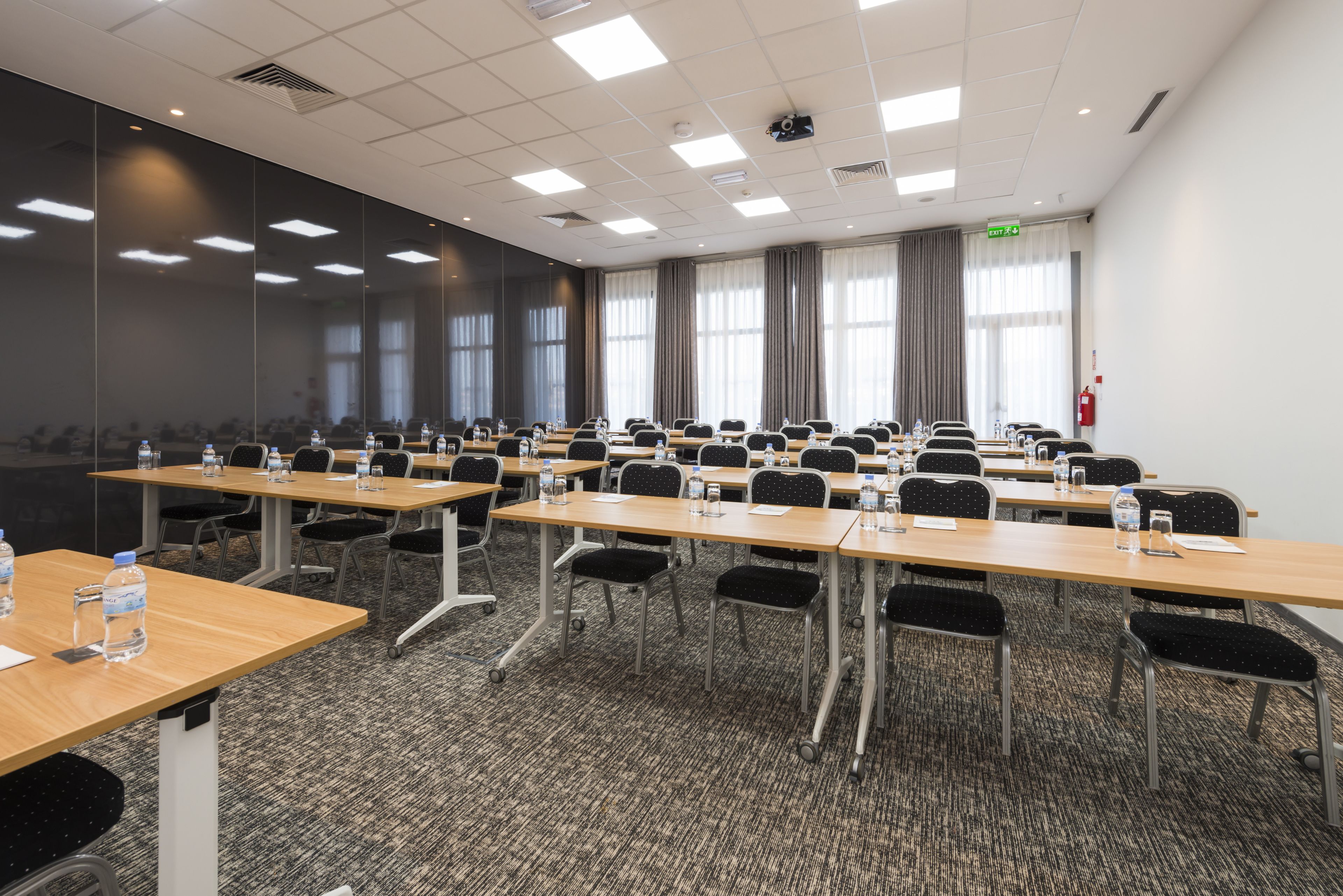 Sala de conferência com várias mesas e cadeiras, equipada com garrafas de água e papéis.