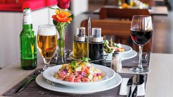 Une table à manger avec une assiette de nourriture, un verre de bière, une bouteille de bière, un verre de vin rouge et des condiments.