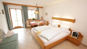 Habitación de hotel con una cama grande, un escritorio con silla, un sofá y una mesita de noche con lámpara.