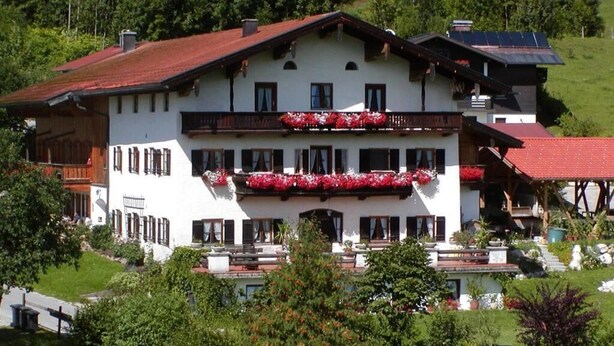 Un edificio de varios pisos con balcones, rodeado de vegetación y un paisaje montañoso.
