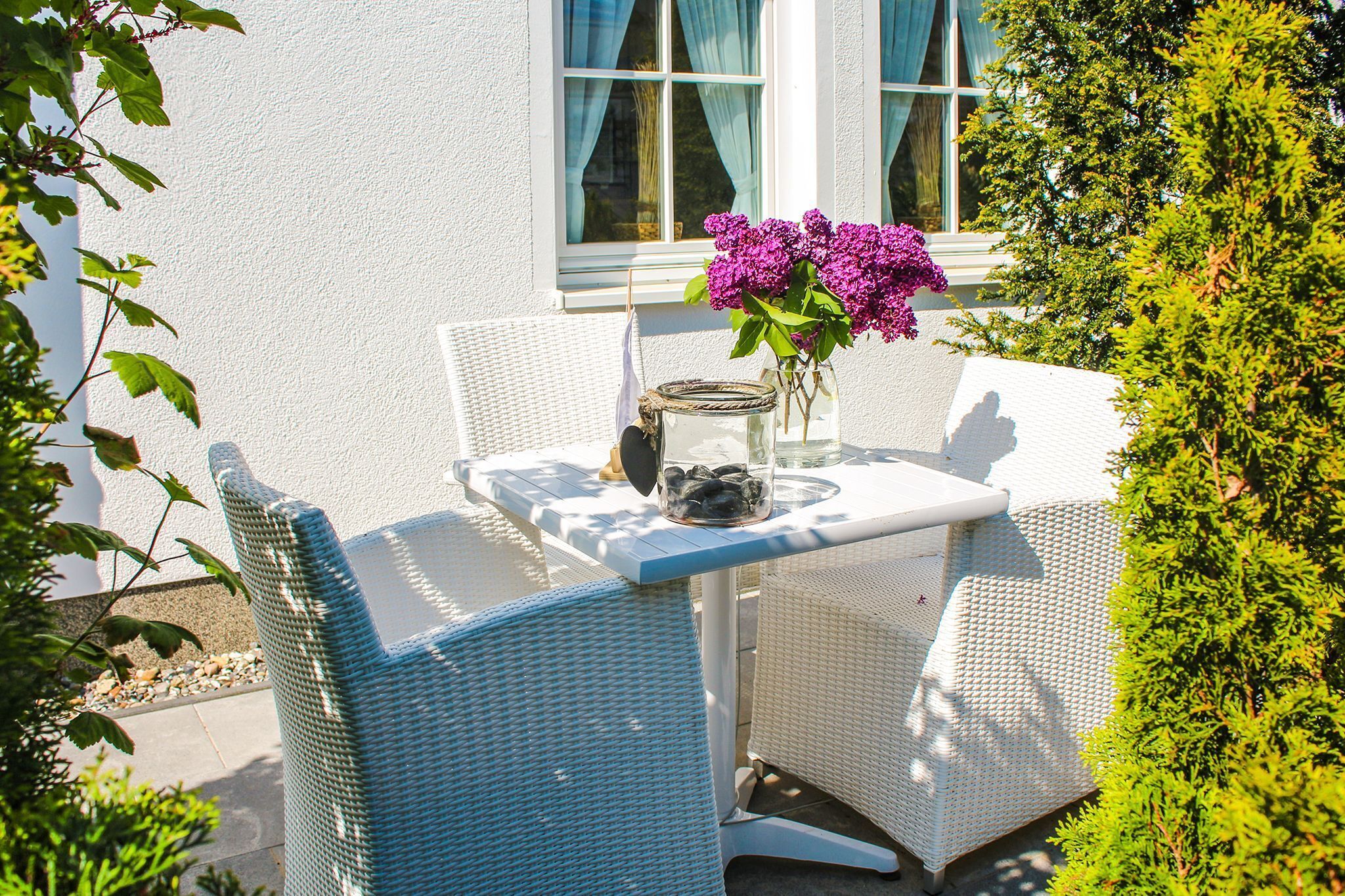 A white wicker table with a vase of purple flowers and a jar of black pebbles.