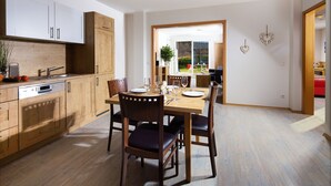 A modern kitchen with wooden cabinets, a Bosch dishwasher, and a dining area with a wooden table and chairs. - Kehlstein, 1-2 Pers., 80 m², Schlafzimmer, Wohnzimmer, Kochnische, Badewanne, Dusche und WC, Terrasse (Bischofswiesen)