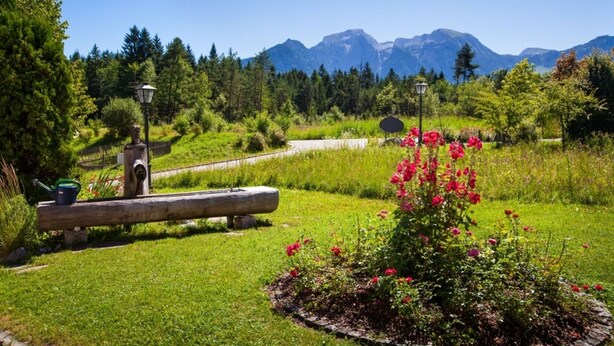 A garden with a wooden bench, a lamppost, and a flower bed with red flowers. - Kehlstein, 1-2 Pers., 80 m², Schlafzimmer, Wohnzimmer, Kochnische, Badewanne, Dusche und WC, Terrasse (Bischofswiesen)