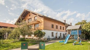 Un grand bâtiment à la façade en bois, doté d’un balcon et d’un toboggan dans la cour.