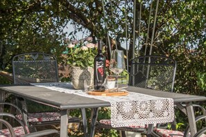 An outdoor dining area with a table set for two, surrounded by wicker chairs with floral cushions. A vase with pink flowers and a bottle of wine are on the table. - Vacation apartment Eiche 64 sqm with balcony (Riedering)