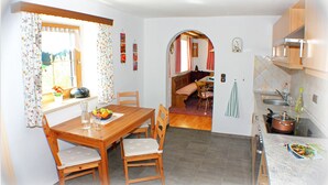 Een compacte keuken met een eethoek, houten meubels en een uitzicht door een boog naar een woonkamer.