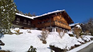 Een houten chalet met balkon, omringd door een besneeuwde omgeving en bomen.